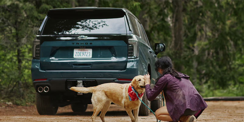 A woman kneels to pet a dog in front of a 2026 Chevrolet Tahoe in Orlando, FL.