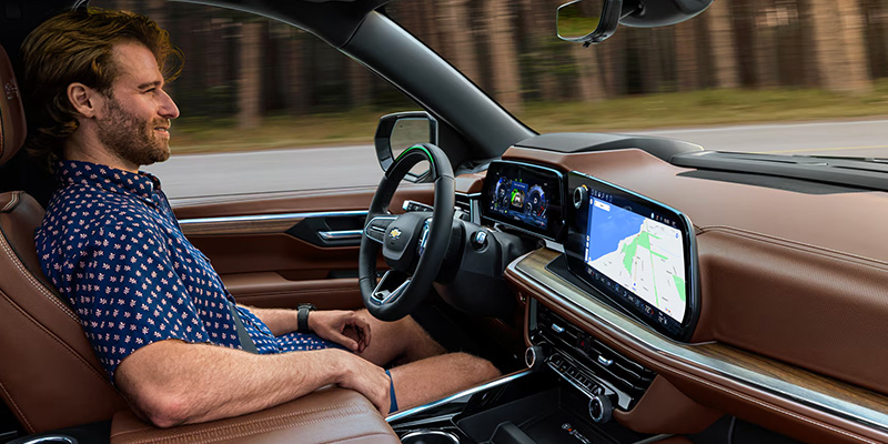 A man sits relaxed in a self-driving car with a brown leather interior, looking content. The dashboard displays a map, conveying a sense of ease and innovation.