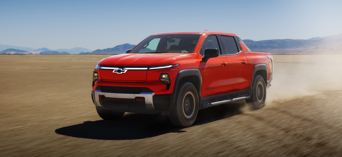2026 Chevy Silverado EV all-electric pickup truck in red driving on an off-road desert trail.